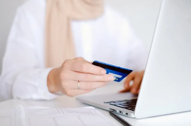 A hand holding a credit card infront of a laptop